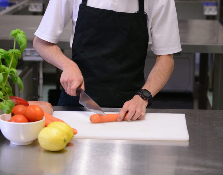 A student using a knife to cut up a carrot.